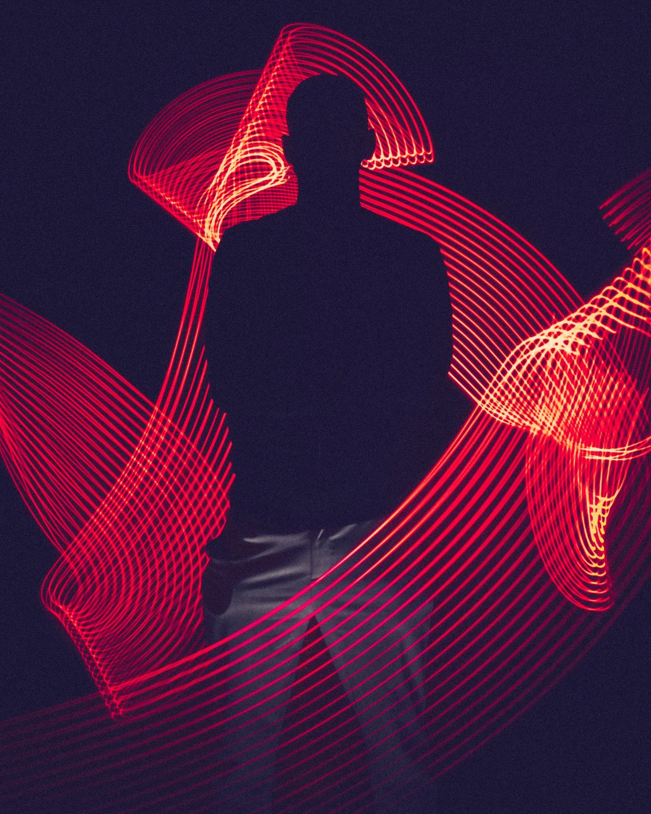 Dark silhouette of a person surrounded by trails of red light, created with light painting