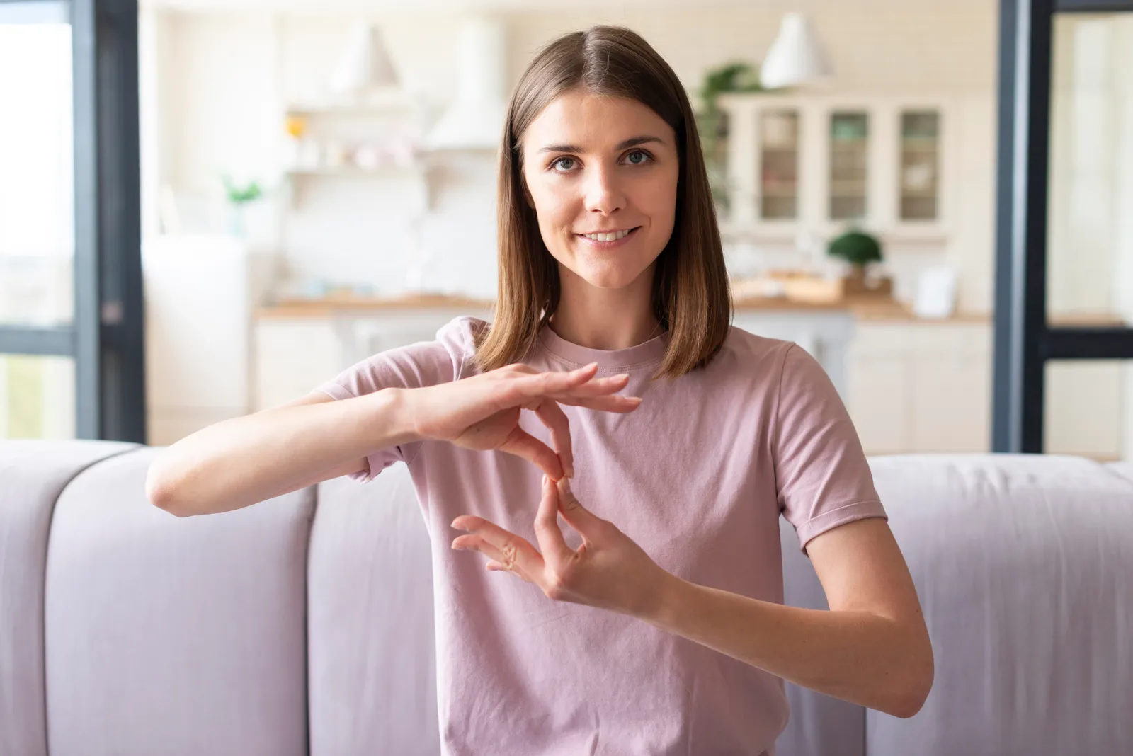 Smiling woman sitting on a sofa, both hands making a sign language gesture