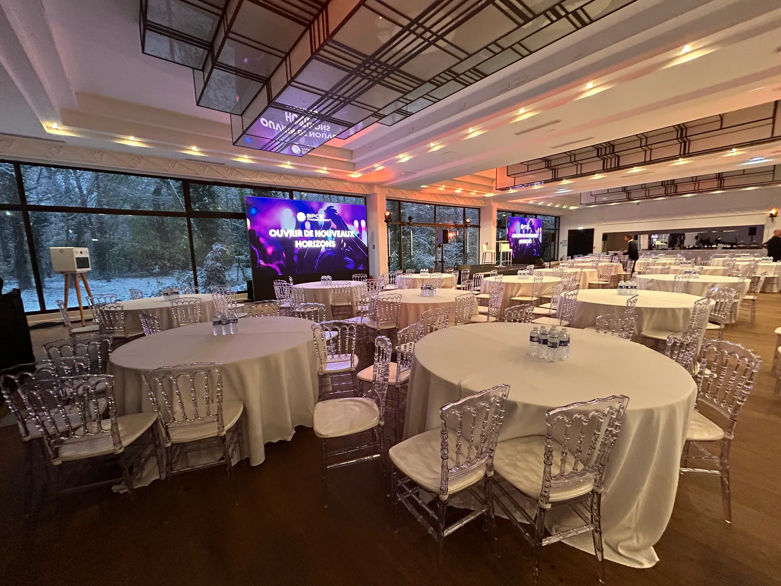 Reception room with round tables and transparent chairs, in front of large LED screens