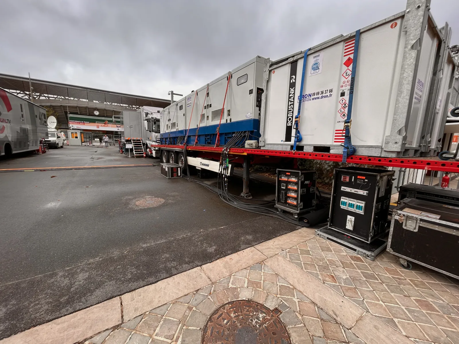 Generators and power distribution cabinets installed on a semi-trailer, next to control-room trucks, in front of a stadium entrance