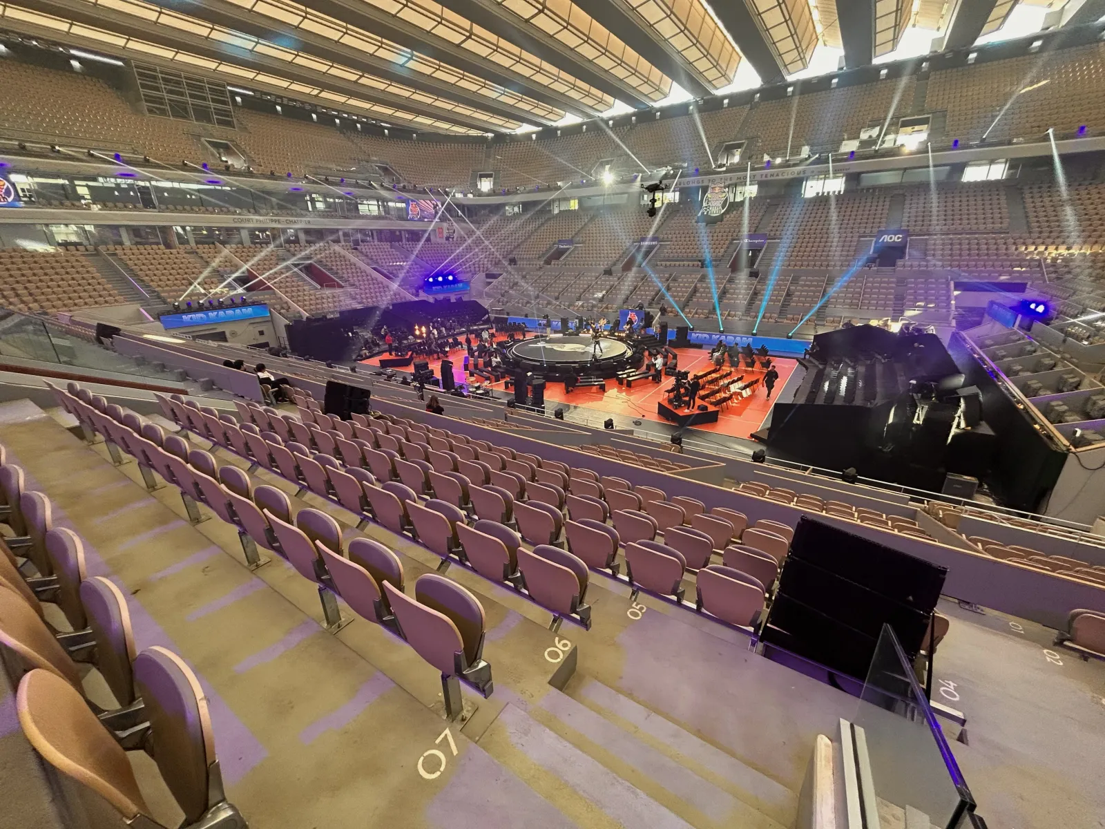 High-angle view of a covered court with a circular stage on the court floor, light beams and screens alongside the stand