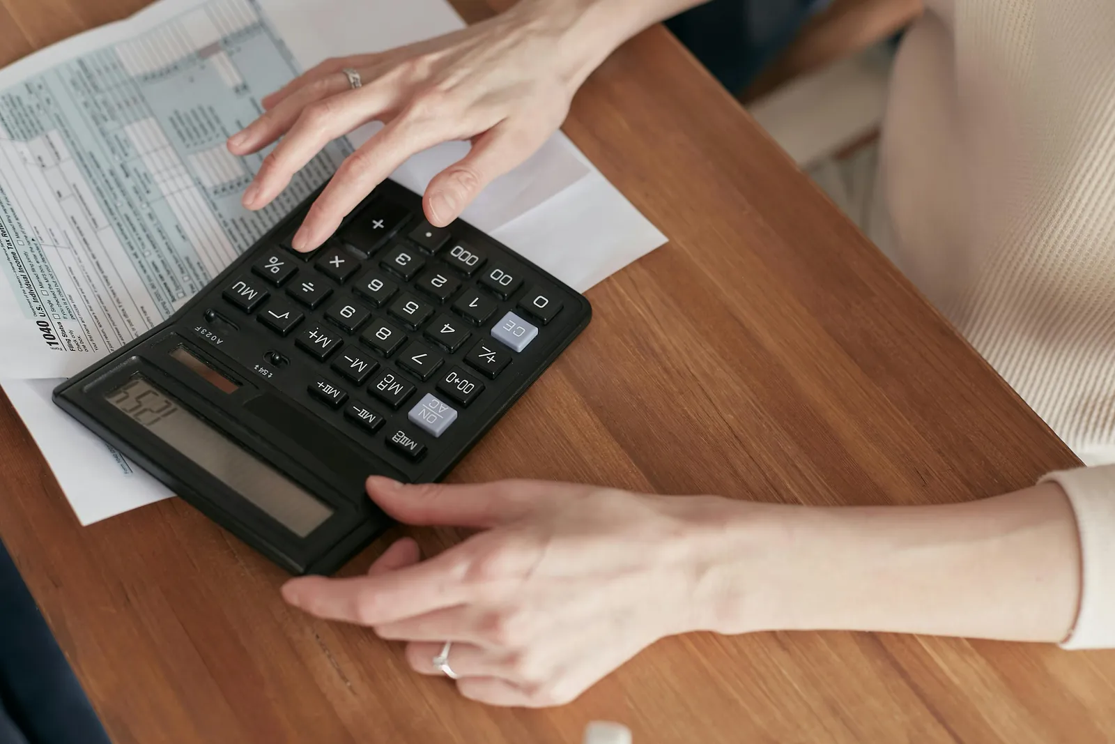 Hands resting on a black calculator next to a form, on a wooden desk