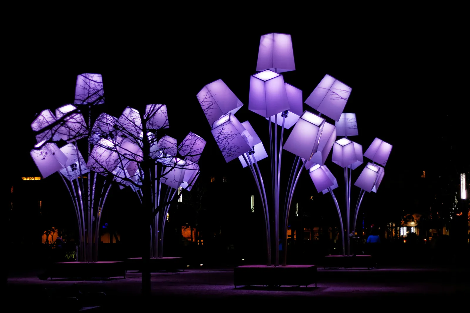 Light sculptures shaped like purple lampshades mounted on tall stems, at night