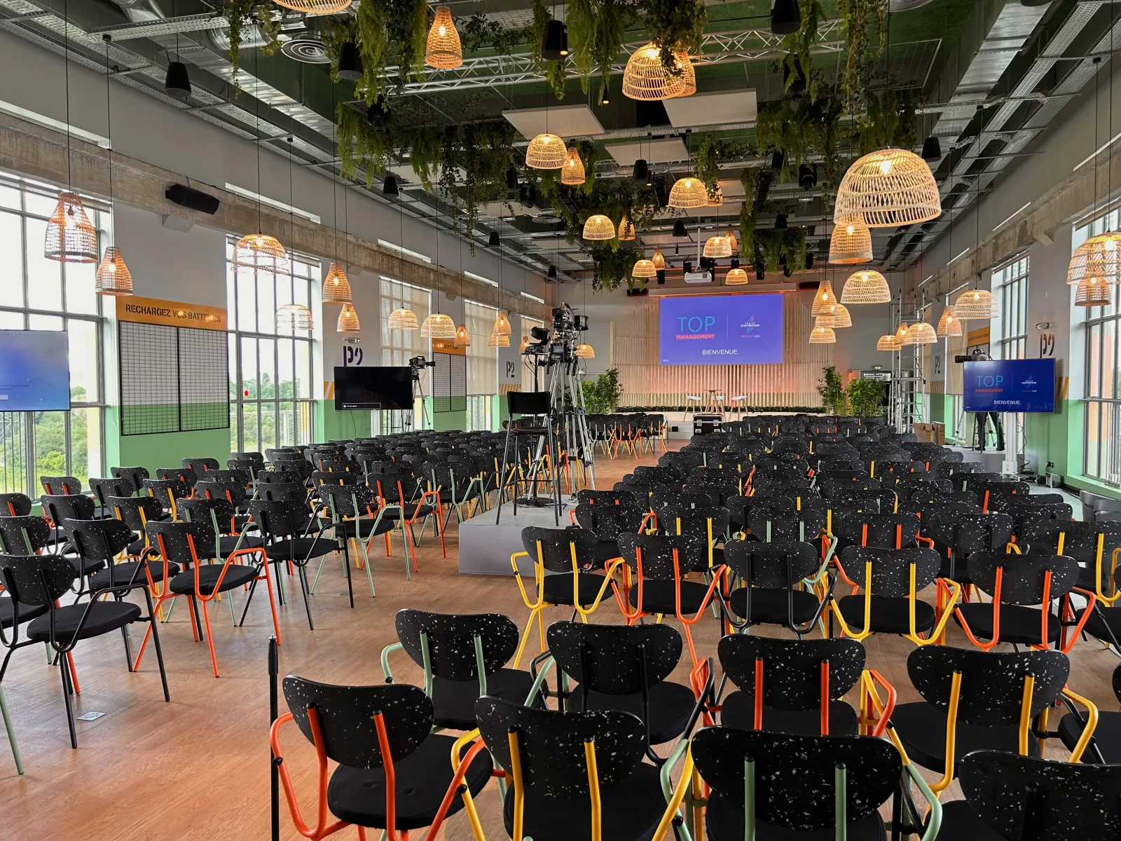 Conference room with black chairs with coloured legs, wicker pendant lights, hanging plants and welcome screens