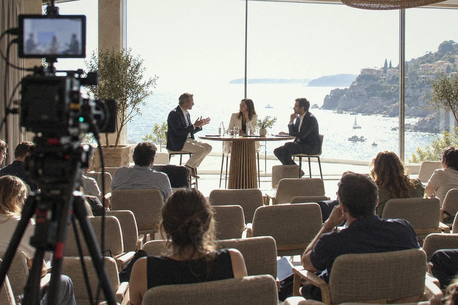 Camera filming a round table in front of a picture window overlooking the sea
